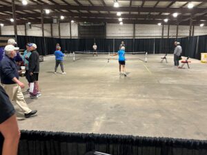 Players engaging in a pickleball game indoors with spectators watching from the sidelines.
